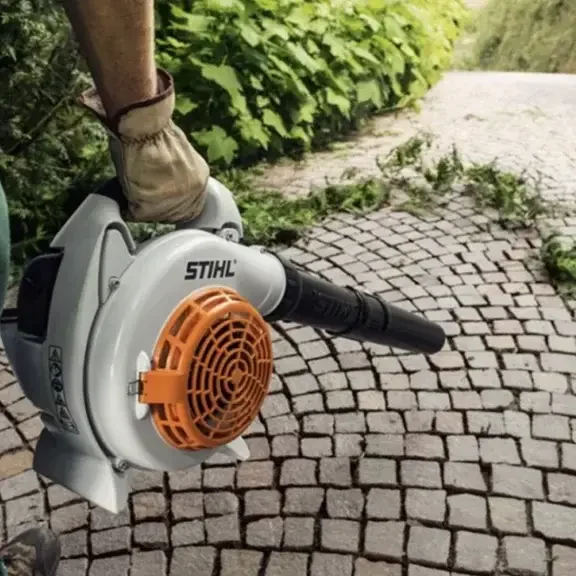 Souffleur de feuilles en action, poignée en main, sur une surface en pavés.
