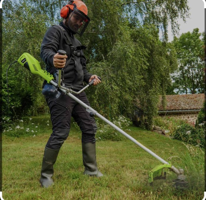 Homme en tenue de jardinage utilisant un débroussailleuse en extérieur.