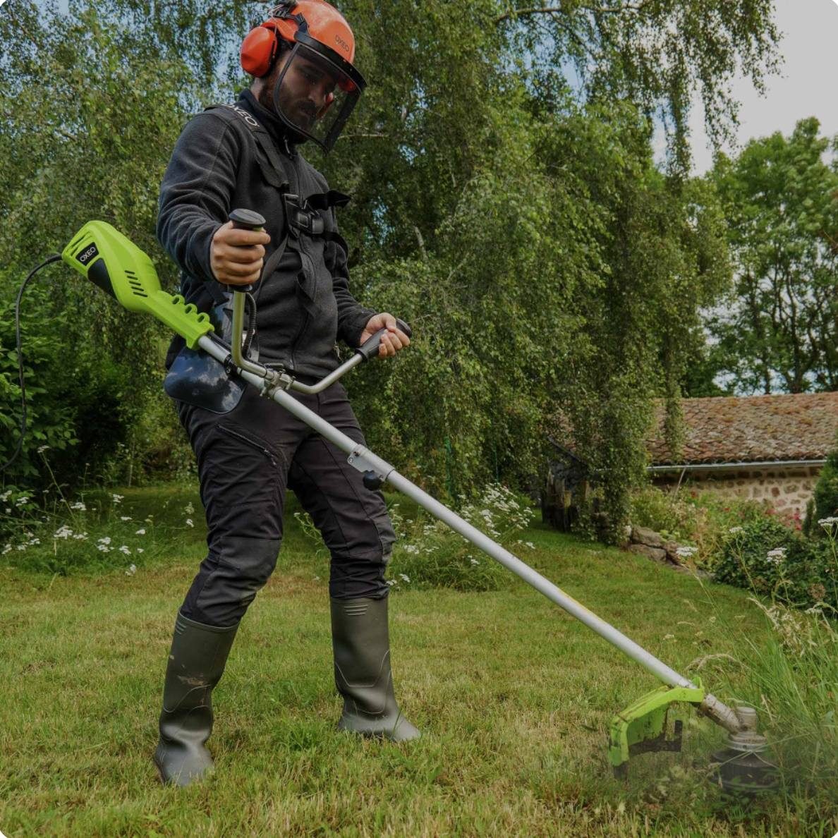 Homme en tenue de jardinage utilisant une débroussailleuse dans un jardin.