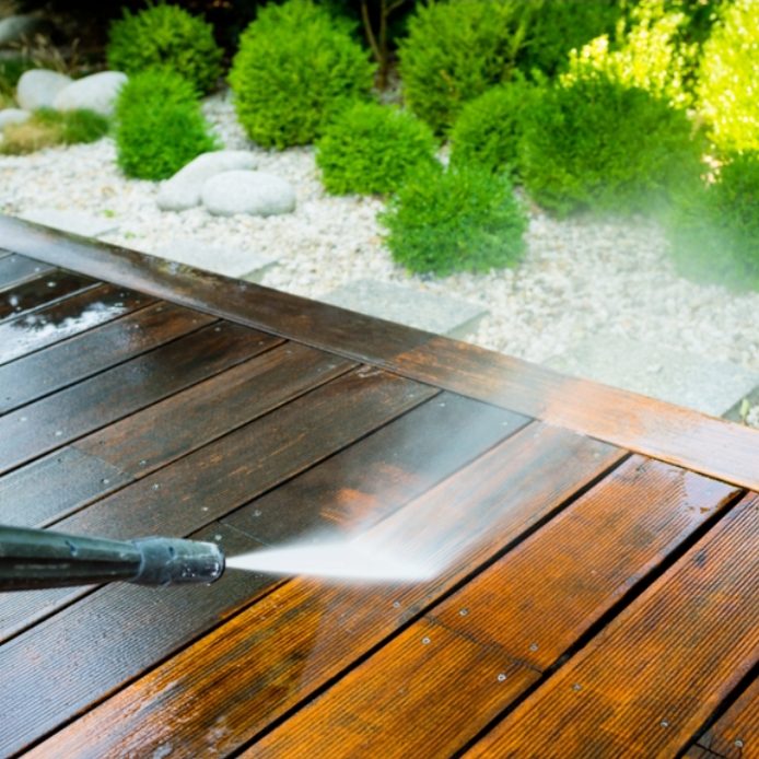 Nettoyage d'un patio en bois avec un nettoyeur haute pression. Verdure en arrière-plan.